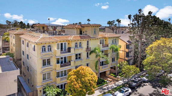 Front view of a multi-story apartment building with balconies and a Mediterranean-style roof.