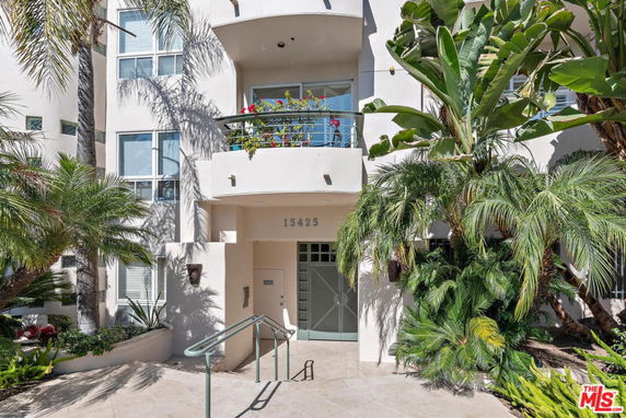 Front view of a multi-story building with a balcony and lush greenery.