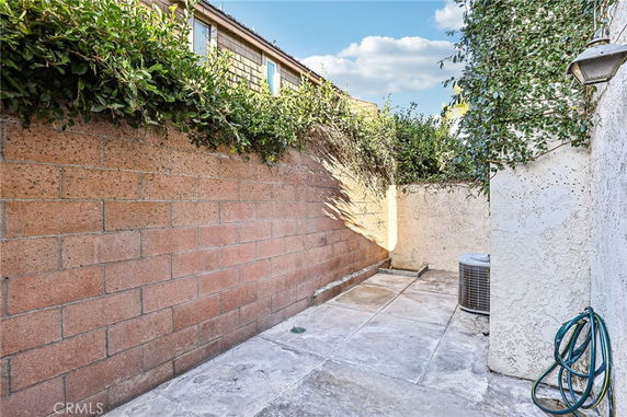 Outdoor area with brick walls, concrete flooring, plants on top of the wall, and an air conditioning unit.