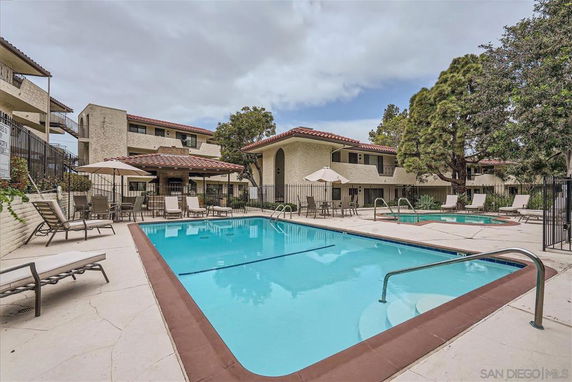 View of a swimming pool area in front of a multi-story building with red-tiled roofs and lounge chairs.