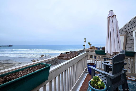 Balcony view overlooking the beach and ocean with a pier in the distance.