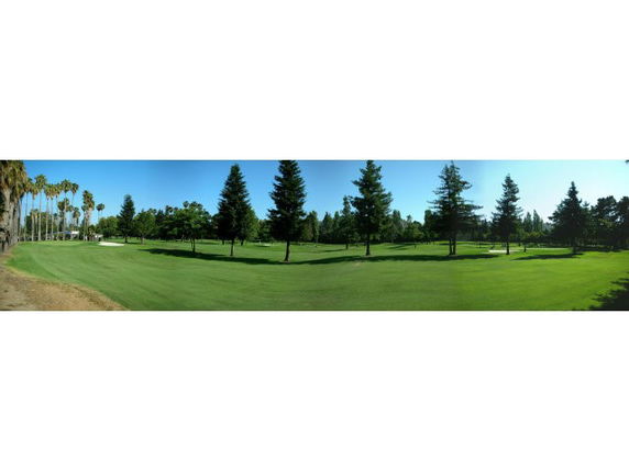 Panoramic view of a golf course with trees and green grass.
