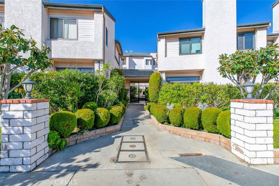 Front view of a two-story residential building with a pathway and hedged entrance.