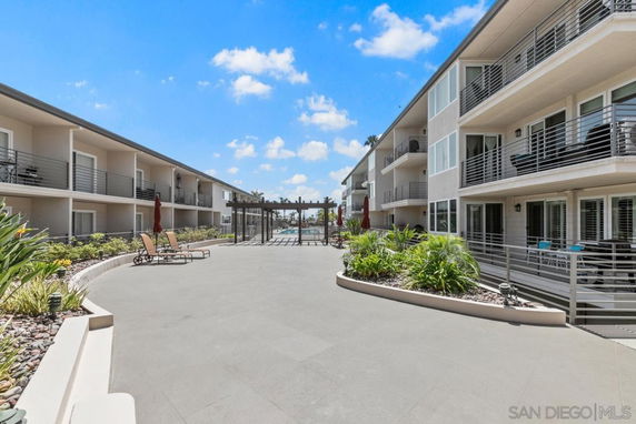 View between two buildings with balconies and a landscaped area.