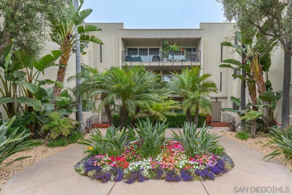 Front view of a modern multi-story building with balconies and lush landscaping.