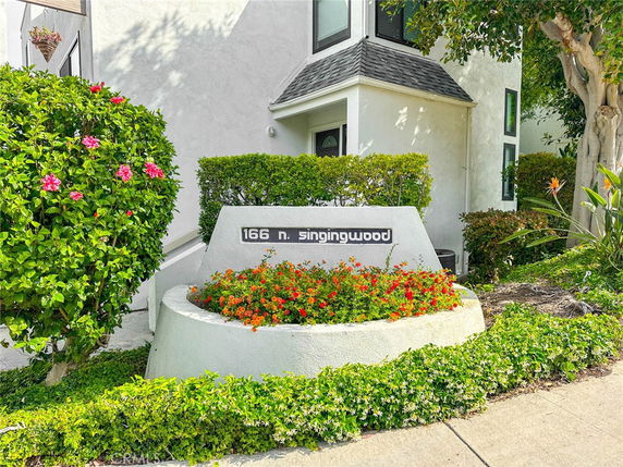 Front view of a building with a sign reading '166 N. Singingwood' surrounded by plants.