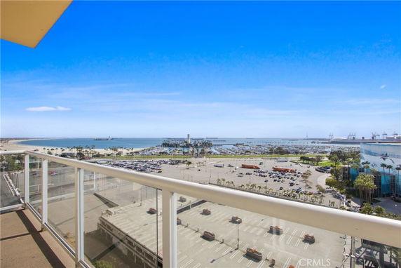 Panoramic view from a high-rise building overlooking a coastal area with a parking lot, marina, and ocean in the distance.