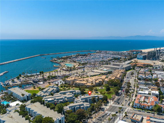 Aerial panoramic view of a coastal cityscape, featuring a marina, buildings, and a vast ocean.