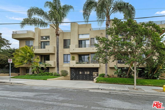 Front view of a multi-story residential building with balconies and palm trees.