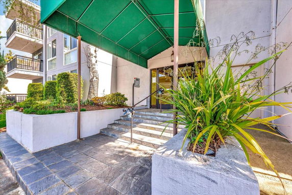Entrance of a building with a green canopy and potted plants.