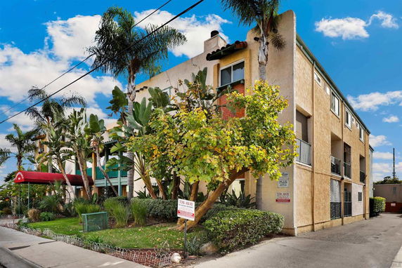 Front view of a multi-story apartment building with balconies and a red awning entrance.