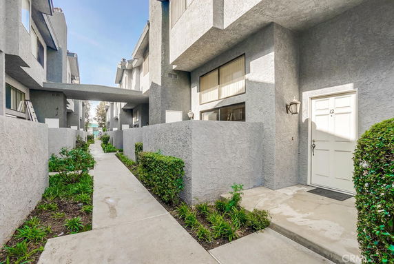 Front view of a row of multi-story houses with a walkway and greenery.
