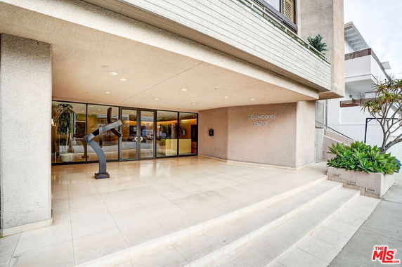 Front view of a building with a covered entrance and a sculpture next to the entrance.