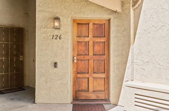 Front view of a house entrance with a wooden door and wall-mounted light.
