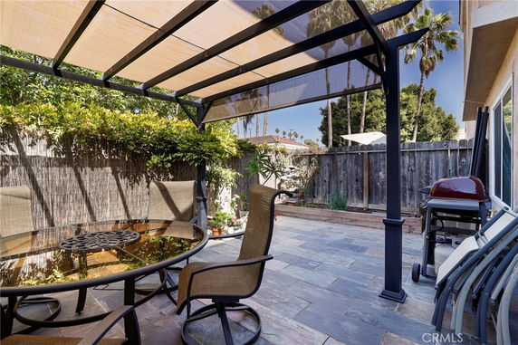Patio area with a table, chairs, and a barbecue grill under a canopy.
