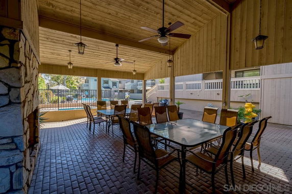 Covered patio area with dining tables and chairs, overlooking a swimming pool.