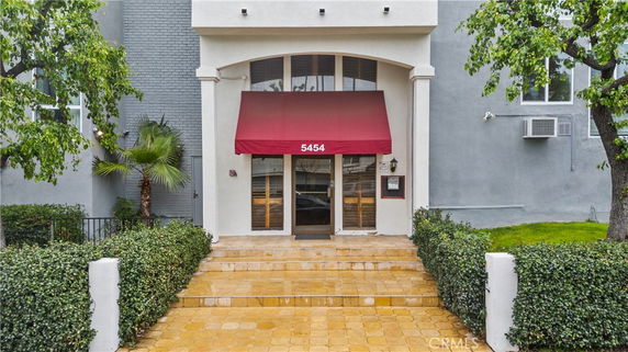 Front view of a multi-story building entrance with a red awning and glass doors.