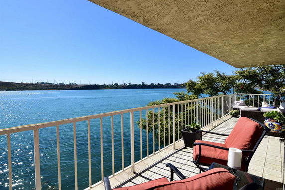 Balcony view overlooking a body of water with trees and distant land visible under a clear blue sky.