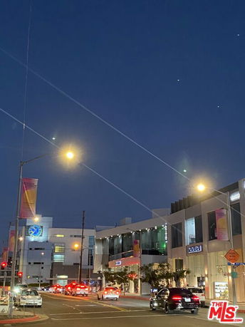 Street view of a modern commercial building at night with cars and streetlights.