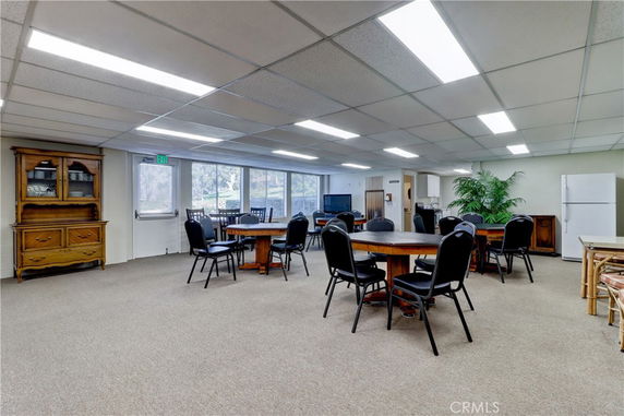 Room with multiple round tables and chairs, cabinets, and a refrigerator, likely used for recreational activities.