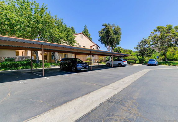 Covered parking area with several parked cars near a building.