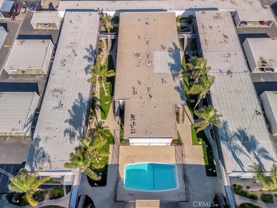 Aerial view of a building complex with flat rooftops. Prominent features include solar panels and air conditioning units. A swimming pool is visible at the bottom center of the image.