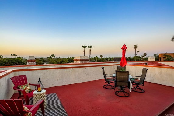 Rooftop with seating area and a red umbrella.