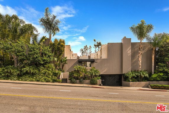Front view of a modern multi-story building with flat roof and surrounding vegetation.