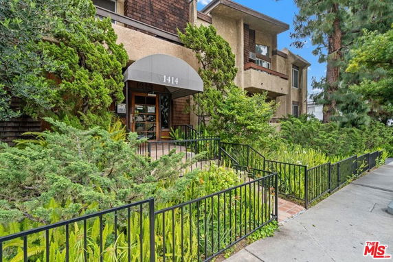 Front view of a multi-story building with an entrance and lush greenery.