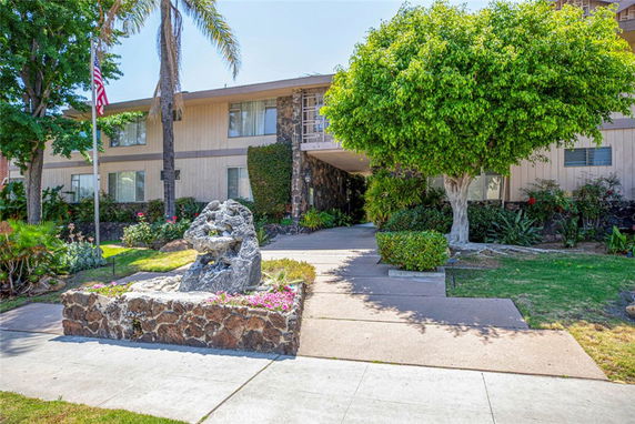Front view of a multi-story residential building with a pathway and a stone sculpture.
