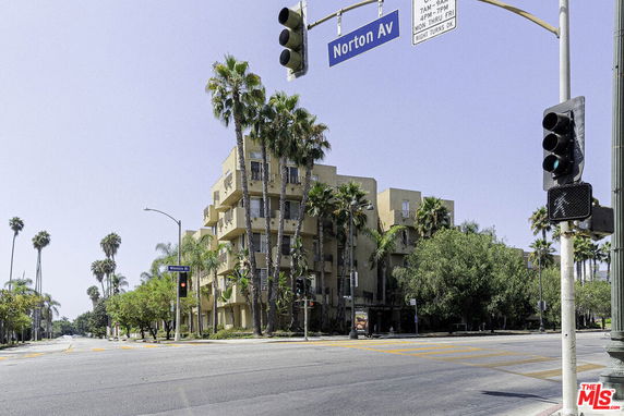 Front view of a multi-story building at a street corner with balconies and palm trees.