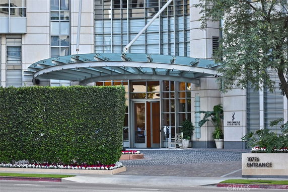 Front view of a modern multi-story building entrance with glass canopy and plants.