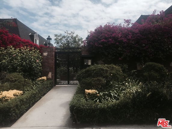 Front view of a gated house with foliage and flowers.