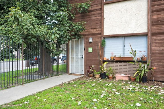 Front view of a two-story building with wooden siding, a metal security door, potted plants, and a window.