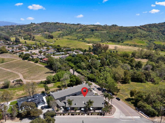 Aerial view of a large building surrounded by greenery and hills in a rural area.