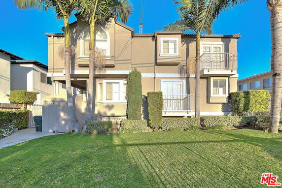 Front view of a two-story house with balconies and palm trees.