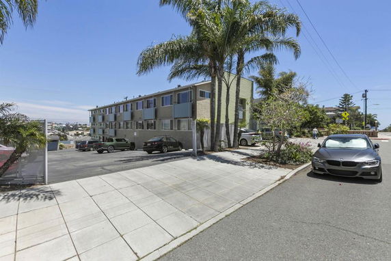 View of a multi-story residential building with an outdoor parking area and parked cars.