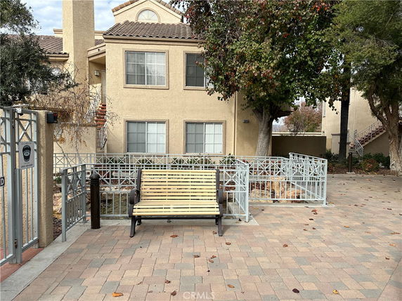 Front view of a two-story house with a tiled roof, large windows, and a bench in the foreground.