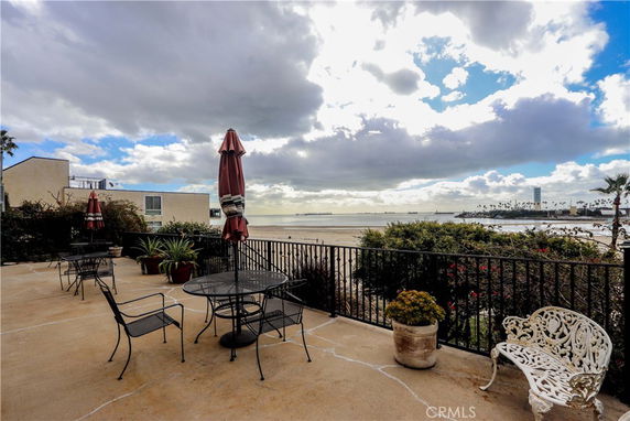 Outdoor patio with tables, chairs, and umbrellas overlooking a beach and ocean view.