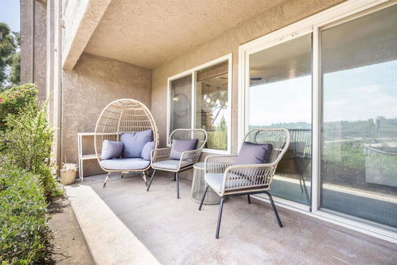 Outdoor seating area with woven chairs and a view of the surroundings through glass doors.