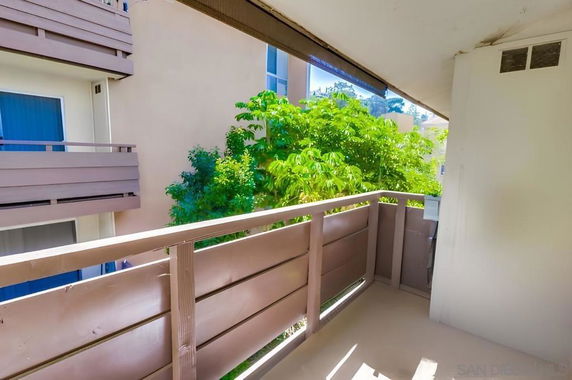 Balcony view with adjacent apartment structures and green trees.