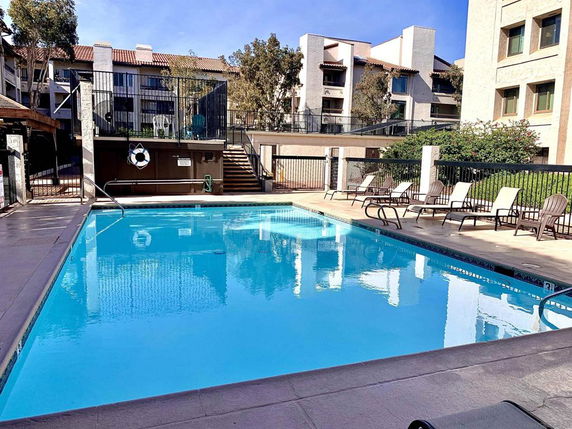 Outdoor swimming pool area with lounge chairs and surrounding apartment buildings.