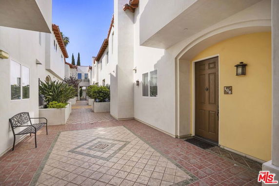 Exterior view of a residential building with a tiled courtyard and entrance door.