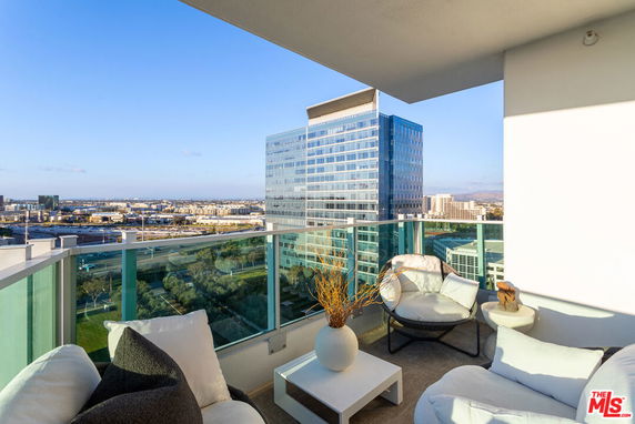 Elevated view from a modern apartment balcony with seating and cityscape in the background.