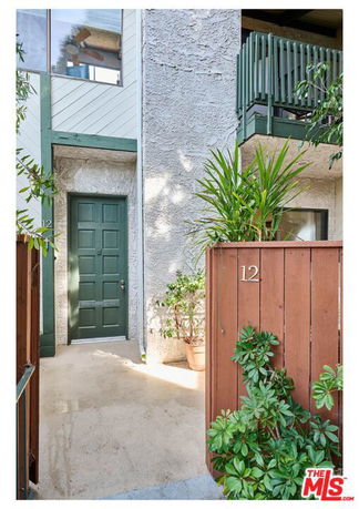Front view of an apartment entrance with a green door and surrounding plants.