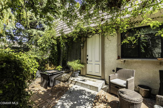 Exterior view of a house entrance with surrounding greenery and outdoor seating.
