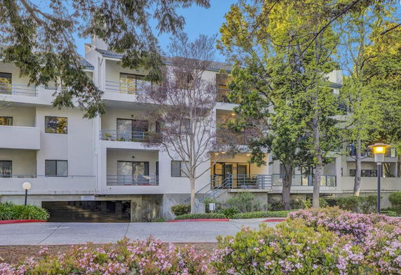 Front view of a multi-story building with balconies and surrounded by trees.