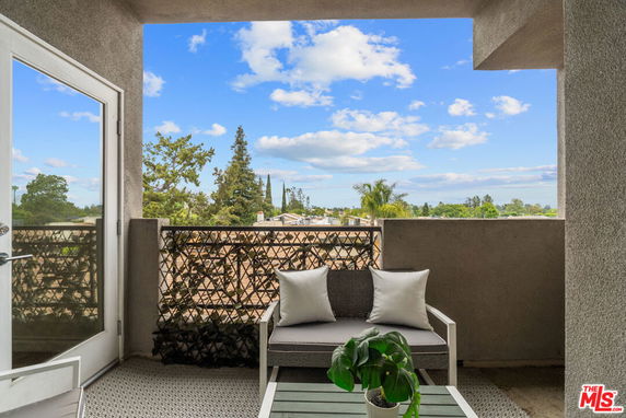 Open balcony with seating area overlooking rooftops and distant trees.