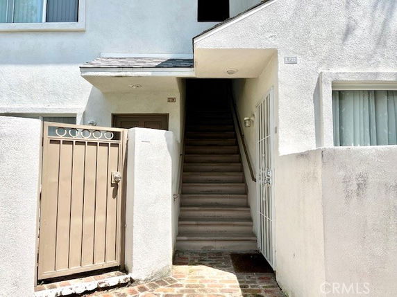 Front view of a building entrance with stairs leading up to a doorway, surrounded by white walls and a small gate.