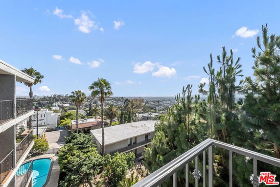 View from a building balcony overlooking surrounding areas with trees and a swimming pool in sight.